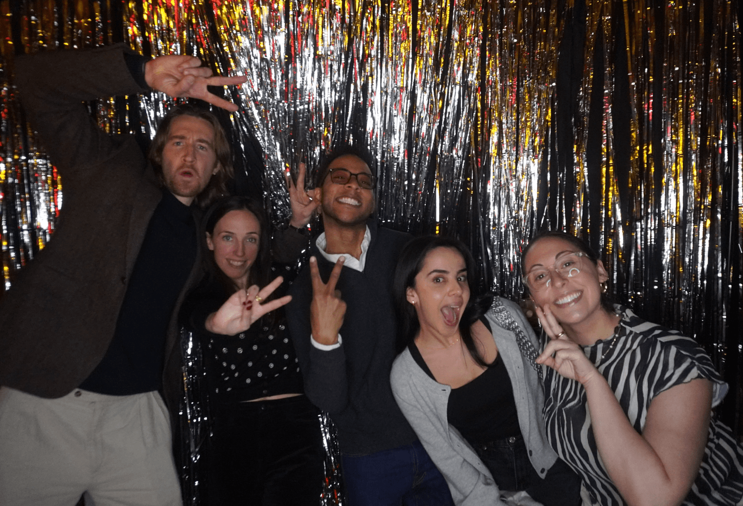 Five friends throwing peace signs in front of a silver tinsel backdrop