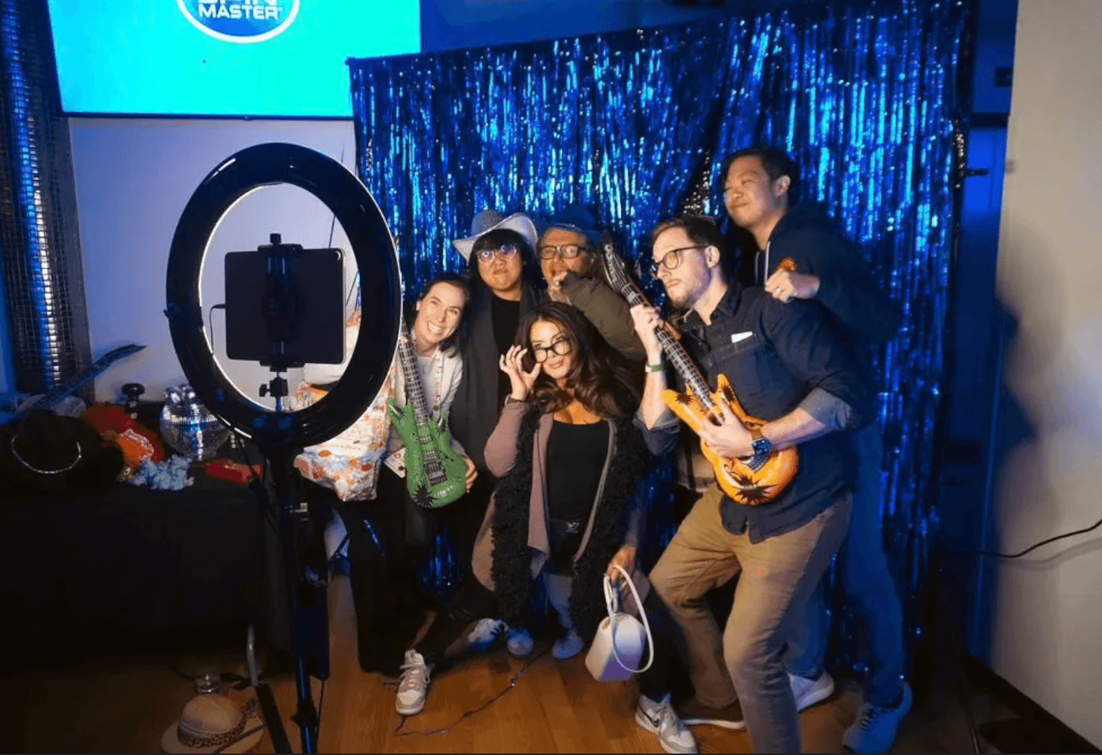 A corporate group posing with inflatable guitars in front of a blue tinsel backdrop