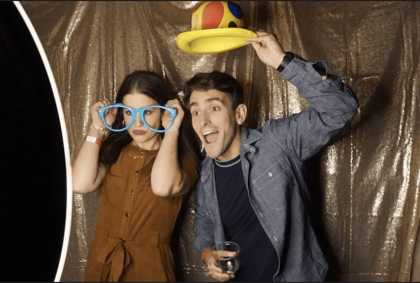 A couple wearing giant novelty glasses in front of a gold sequin backdrop