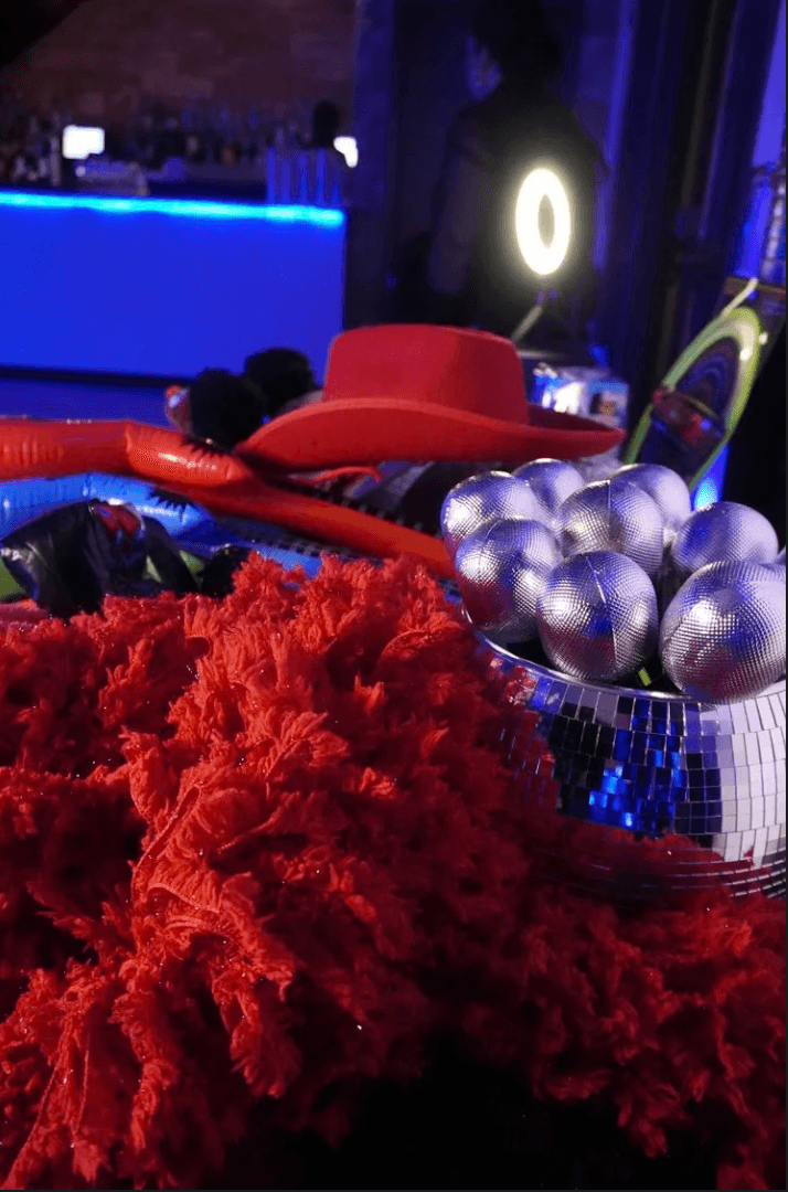 A photo booth prop table with a red hat, disco ball and feather boa
