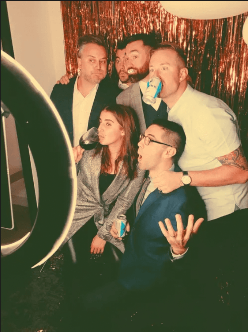 A group of six making funny faces in front of a red tinsel backdrop